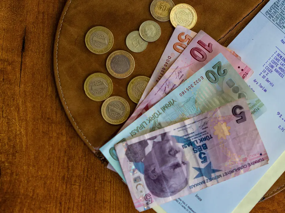 Gün sonu kasa sayımında deri cüzdanın üstünde Türk lirası banknotlar, madeni paralar ve fiş