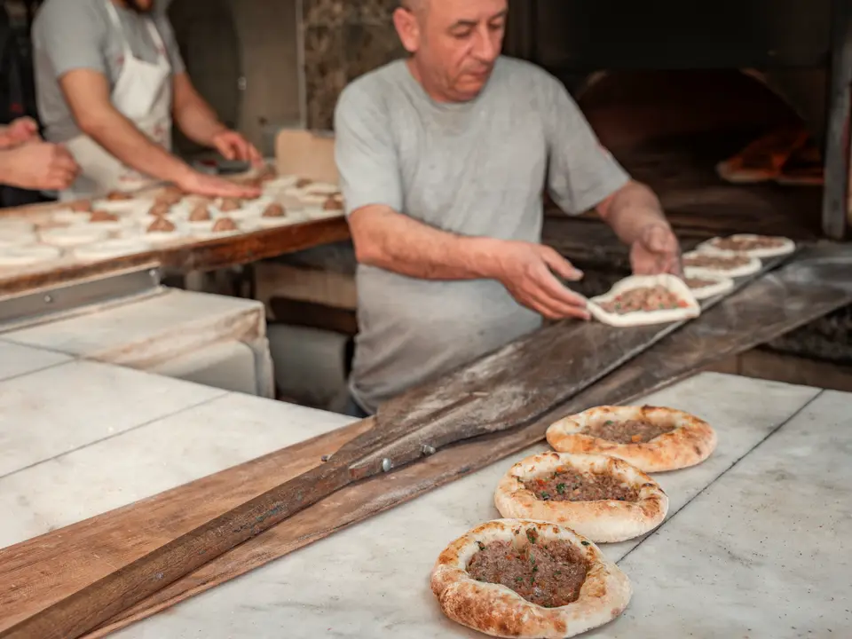 Pide fırınının mermer tezgâhında kıymalı pideleri sıraya dizen usta, arkada hamur açan yardımcısı